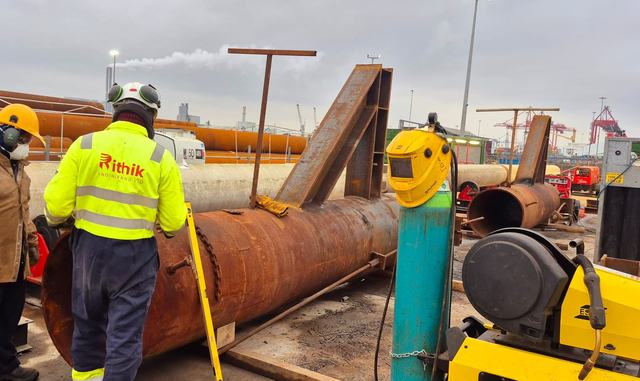 A Rithik crew member in a hi-vis jacket beside a large steel pipe