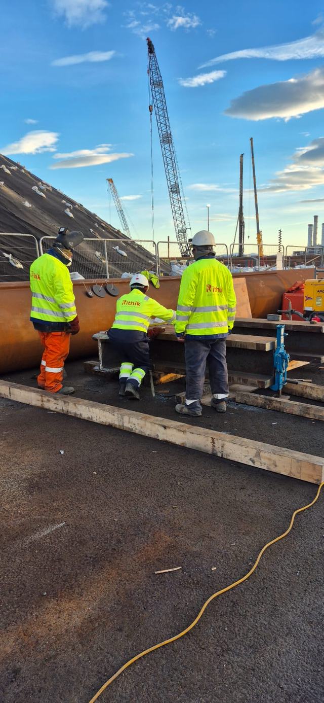 Crew members working on a large pipe beside a crane